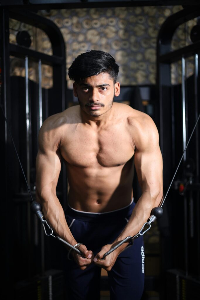 Strong shirtless man in gym focused on chest workout using cable machine.